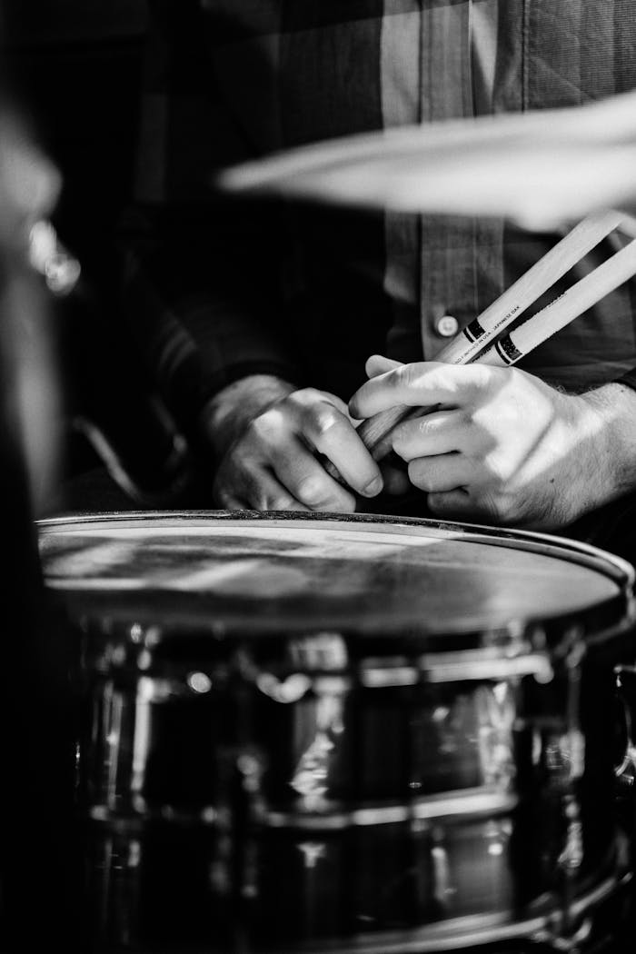 Artistic black-and-white photo showing a drummer's hands on a snare drum in a close-up view.